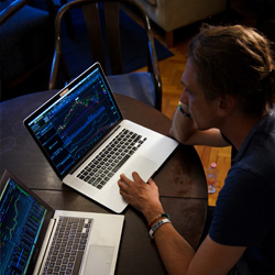 A man considers the data on one of two open laptops on the table before him.