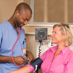 A nurse checks the blood pressure of a patient in a small exam room